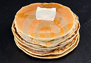 Stack of pancakes in syrup on dark background