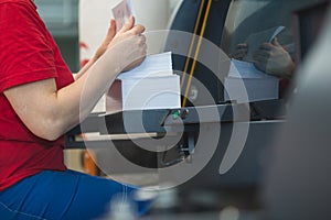 Stack of paper in hands of female worker in front of printing press machine