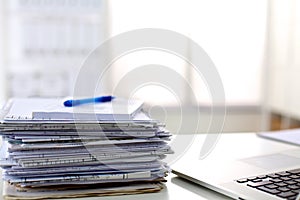 A stack of papers on the desk with a computer