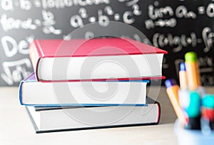 Stack and pile of books on table in front of a blackboard