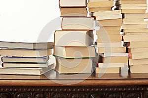 Stack of piled books rest on a wooden table with copy space for your text