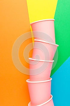 Stack of pink paper drinking cups on multicolored pinwheel background. Funky retro style. Birthday party fest celebration kids fun photo