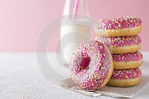Stack of pink and white donats with bottle of milk over white ba