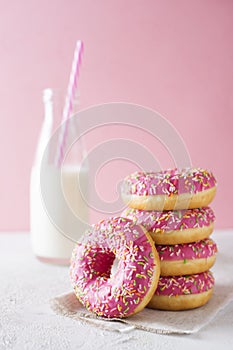 Stack of pink and white donats with bottle of milk over white ba