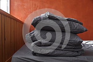 A stack of plain pillows, blankets on the bed. Gray linens on red wall background