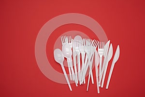Stack of plastic forks and spoons on red background, top view