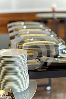 Stack of plates next to closed chafing dishes