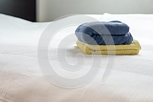 Stack of plush hotel clean soft towels White,Blue,Yellow towel on bed decoration in bedroom interior