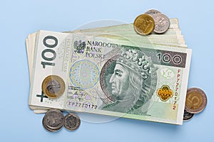 Stack of polish paper currency, 100 zloty PLN bills and coins, on blue background