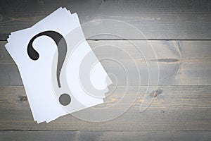 Stack of question marks printed on white paper on a gray board background