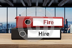 stack of red and black office binder file folder on wooden desk in large modern office building with skyline view hire fire label
