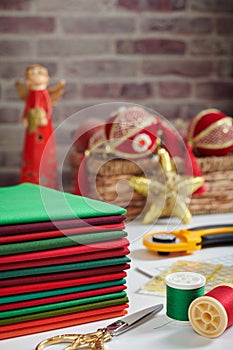 Stack of red and green fabrics, sewing and quilting accessories on Christmas decorations background