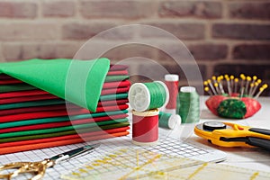 Stack of red and green fabrics surrounded by sewing and quilting accessories on brick wall background