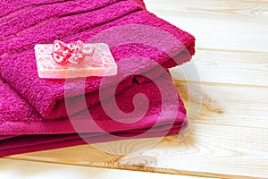 Stack of red terry towels and piece of rose soap with fabric flower on it, lied on wooden table