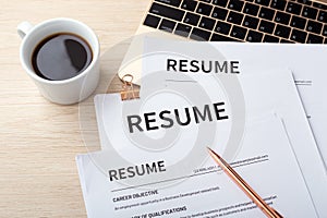 Stack of resumes on laptop with pen and coffee cup