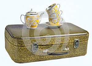 A stack of retro cups and a ceramic teapot on old leather suitcase isolated on a white background.