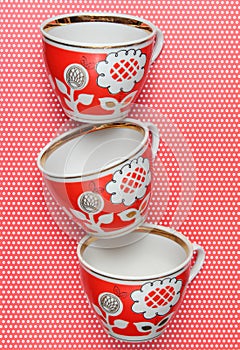 Stack of retro cups with red patterns on a tablecloth whith polka dots.