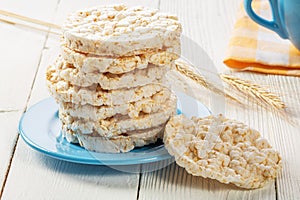 A stack of rice biscuits on a blue saucer and ears of barley on a wooden table