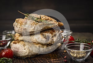 Stack of roast chicken breast with fried seasoning and tomatoes on dark wooden background