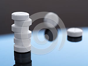 A stack of round tablets and two pills separately on a mirror surface. Medical background with medicines for business, industry photo