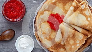 Stack of russian thin pancakes blini with red caviar and fresh sour cream.