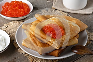 Stack of russian thin pancakes blini with red caviar on an old wooden table. Maslenitsa, traditional Russian blini