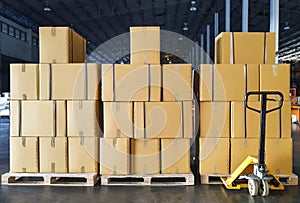 Stack of shipment package boxes on wooden pallets and hand pallet truck in interior warehouse storage.