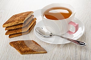 Stack of shortbread cookies with sugar and cinnamon, cup of tea, spoon on saucer on table