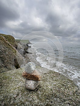 Stack of small rocks on a big stone, beautiful ocean scene in the background with cloudy sky. Relaxation and zen concept