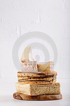 Stack of soft French cow`s milk cheese on a cutting board on white. Camembert, Livarote, Pont-L`eveque cheese from Normandy. Cop