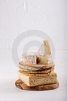 Stack of soft French cow`s milk cheese on a cutting board on white. Camembert, Livarote, Pont-L`eveque cheese from Normandy. Cop