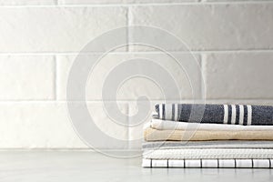 Stack of soft kitchen towels on table near brick wall, space for text