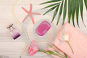 Stack of soft terry towels with pink flowers, soap, bottle of perfume, sea star and green leaves on wooden background.