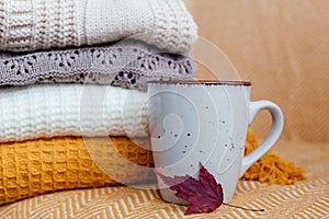 Stack of soft warm plaids, a mug and an autumn leaf close-up.