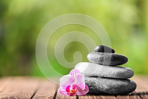 Stack of spa stones and beautiful flower on wooden table against blurred background