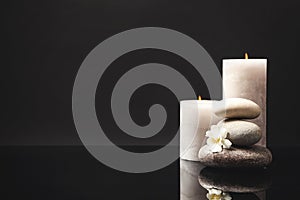 Stack of spa stones, burning candles and fresh flower on mirror surface. Space for text