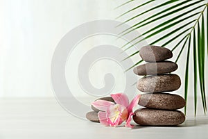 Stack of spa stones, palm leaf and flower on table against white background