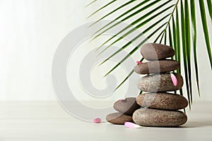 Stack of spa stones, palm leaf and petals on table against white background