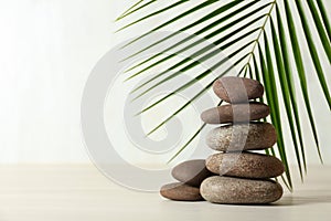 Stack of spa stones and palm leaf on table against white background