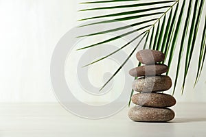 Stack of spa stones and palm leaf on table against white background