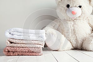 Stack of spa towels on white wooden table with white soft toy bear on background. Childrens washing concept