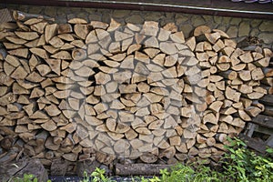 Stack of split firewood logs against stone wall under metal roof