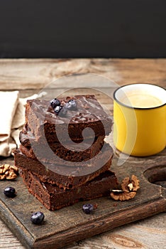 Stack of square baked slices of brownie chocolate cake with walnuts on a wooden surface