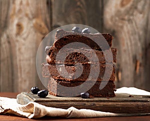 Stack of square baked slices of brownie chocolate cake with walnuts on a wooden surface