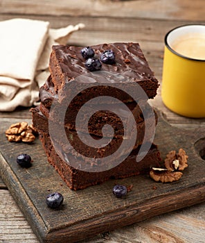 Stack of square baked slices of brownie chocolate cake with walnuts on a wooden surface. Cooked homemade food. Chocolate pastry