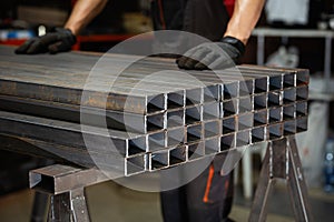 stack? of square? metal tubes? profile or pipes for construction supplies and welding works with worker on background