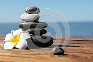 Stack of stones and flower on wooden pier near sea. Zen concept