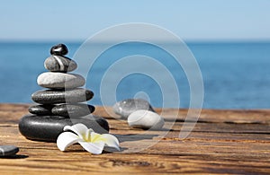Stack of stones and flower on wooden pier near sea. Zen concept