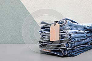 Stack of stylish jeans with tag on table
