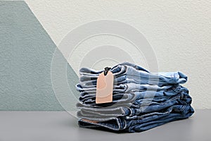 Stack of stylish jeans with tag on table